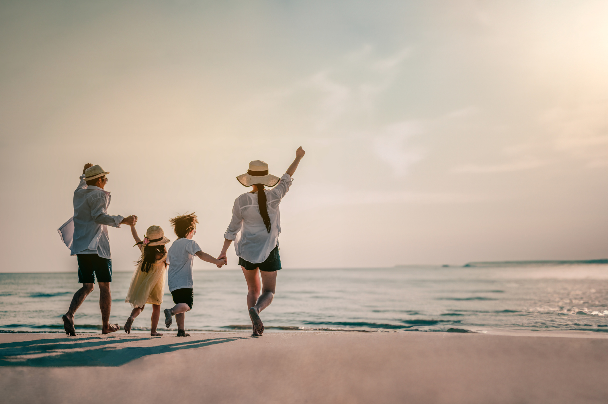 Happy Family Consisting Of Father, Mother, Son And Daughter Having Fun Playing On The Beach During Summer Vacation On The Beach.